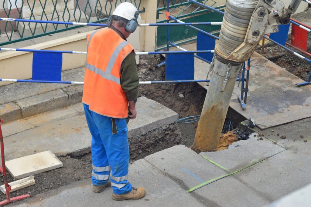 Asphalt worker in uniform controls the drilling process. Breaking concrete at road construction site — Photo